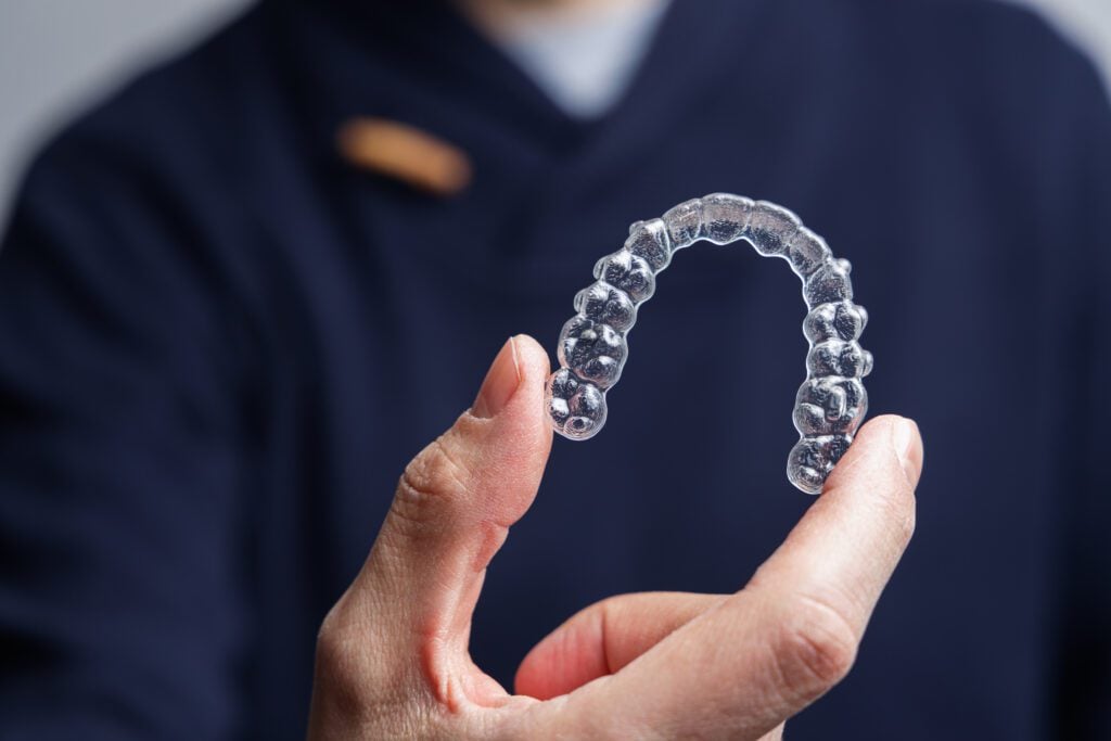 An Invisalign clear aligner being held up by a dentist.