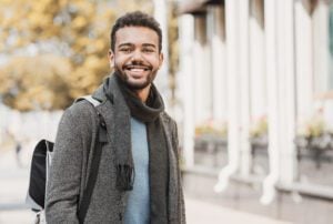 A young man smiling while walking outside, wearing a backpack.