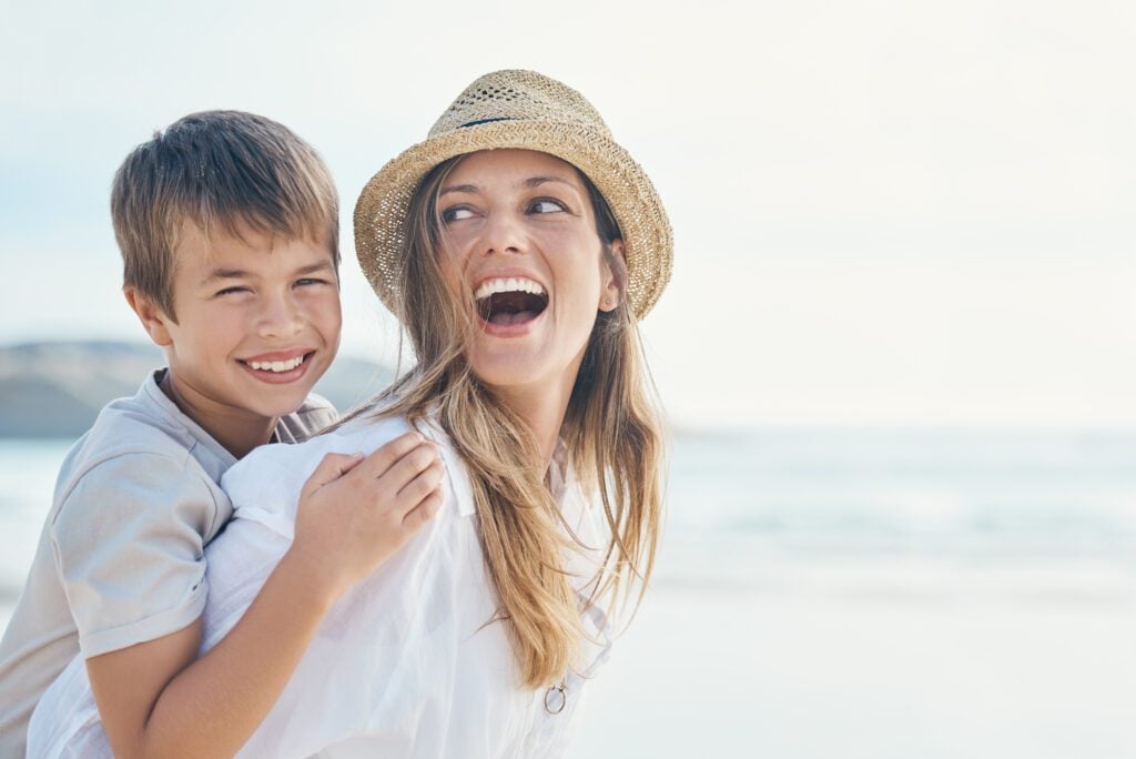 A young woman and a child smiling while enjoying a day at the beach.