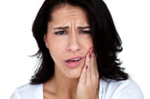 A woman grimaces in pain, holding her cheek, indicating a severe toothache.