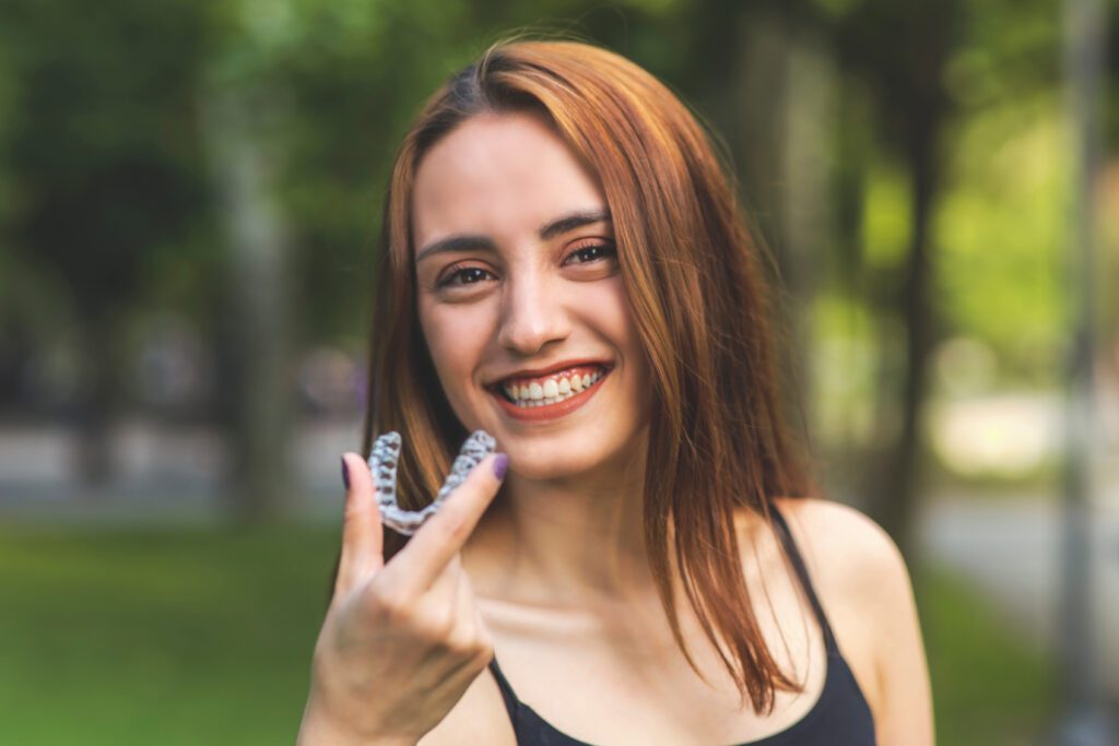 A young woman holding a clear aligner, proudly displaying her straight teeth.