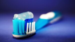 Close-up of a toothbrush with blue bristles and toothpaste against a blue background.