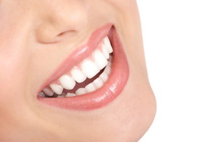 Close-up of a person's smile showing white teeth and glossy pink lips.